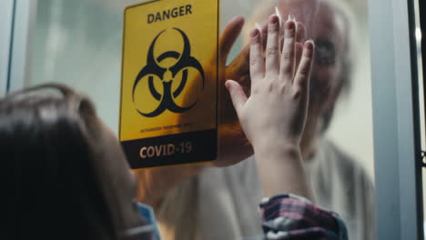 family members touching hands through glass during covid-19 pandemic