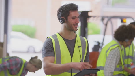 gerente masculino con auriculares en el almacén de distribución logística usando una tableta digital
