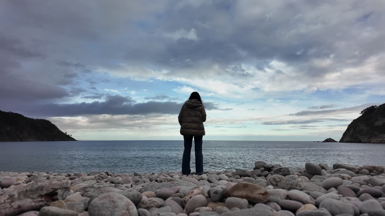 Person standing alone facing the ocean on a rocky beach