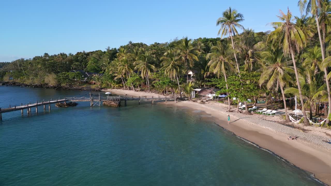chica caminando descalza en vestido verde a lo largo de una playa vacía