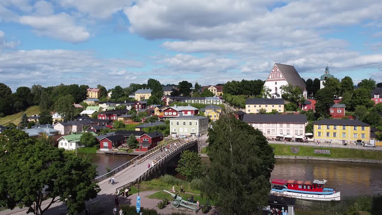 Luftfoto i fugleperspektiv over smukt finsk bybillede med farverige bygninger, turister går på bro over floden om sommeren.