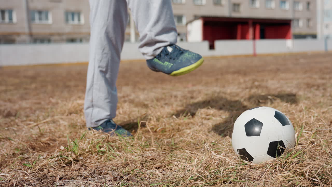 El jugador coloca el pie con cuidado, el atleta experto alinea el pie meticulosamente antes de ejecutar un potente disparo, el jugador experimentado se acerca al balón con una postura firme en un campo de fútbol local muy usado.