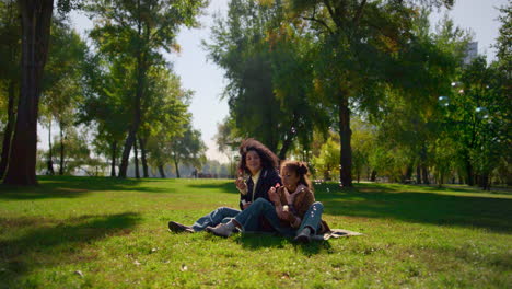 madre de niño alegre soplando burbujas de jabón en el parque soleado. picnic familiar en el día de primavera