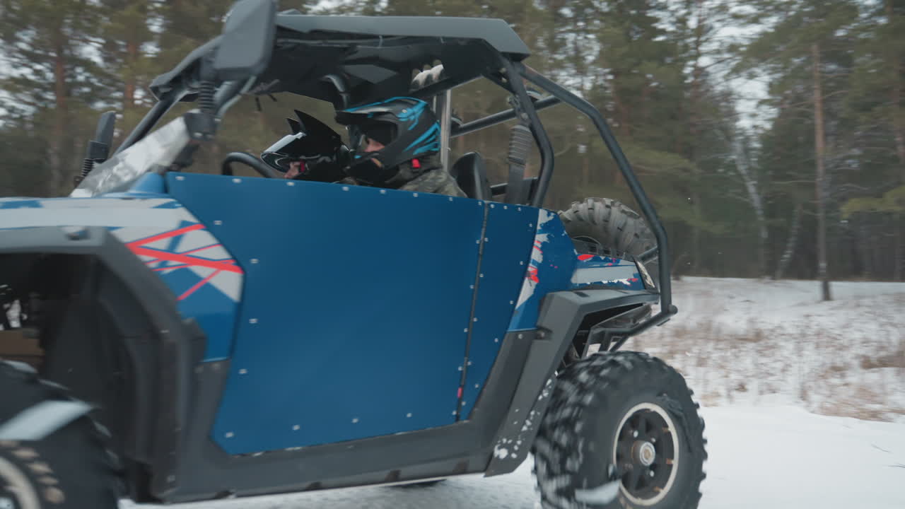 ATV che si dirige verso la telecamera attraverso la neve, fari che brillano con il bagliore del tramonto, pilota che guida un robusto buggy fuoristrada, posto di controllo con cartello stradale visibile, slancio dinamico e tono avventuroso e urgente.