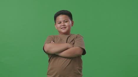 an asian boy crossed arms and warmly smiling on green screen background in the studio