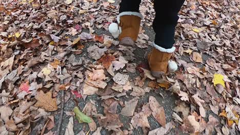 close up follow of a little girl's leather boots with faux fur as she runs down a leaf covered path and falls over slow motion