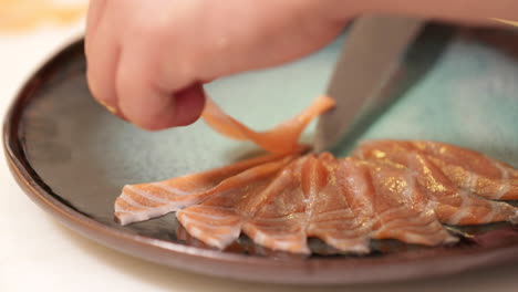 arranging slices of raw salmon fish in a plate - sashimi preparation - close up