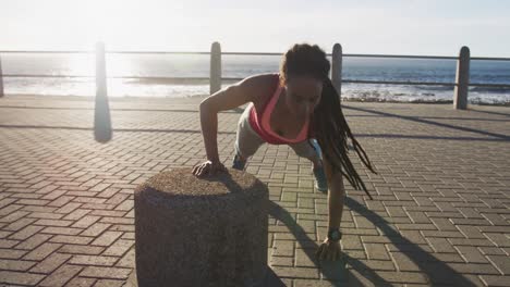 african american woman in sportswear doing press ups on promenade by the sea