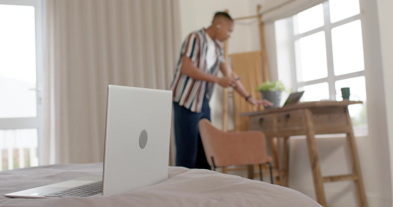 Uomo afroamericano che entra con il telefono, lo posiziona sulla scrivania, digita sul laptop, con spazio per il testo.