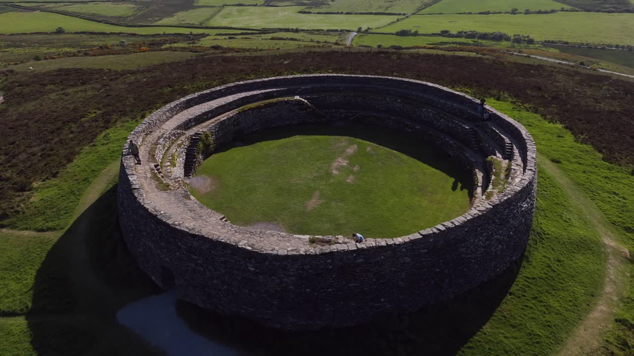 Grianan of Aileach, County Donegal, Ireland, June 2023. Drone orbits counter clockwise around the historic stone monument surrounded by green fields with tourists exploring the iconic Gaelic Ringfort.
