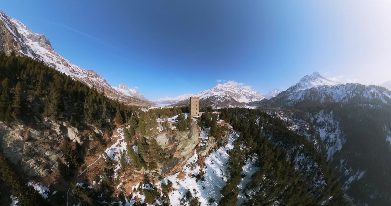 Storica Torre Belvedere in pietra su una collina rocciosa circondata da montagne innevate al Passo del Maloja nelle Alpi Svizzere. Vista panoramica aerea con drone, spazio per il testo.