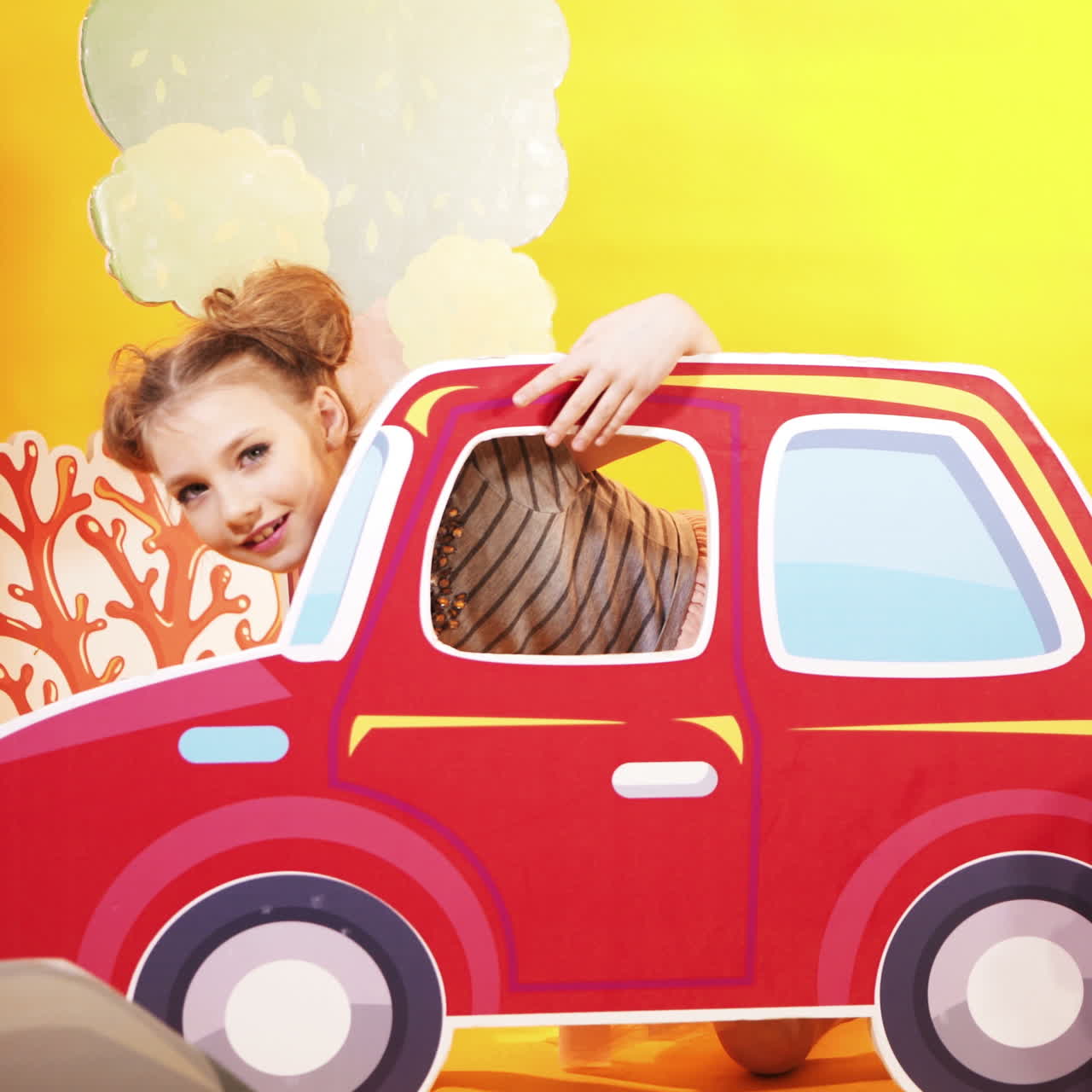 Simpatica bambina su uno sfondo di parete giallo brillante. Una bella bambina si diverte con una grande macchinina giocattolo. Video quadrato