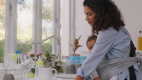 madre feliz sosteniendo al bebé trabajando en casa lavando platos limpiando la cocina cuidando al niño haciendo tareas domésticas disfrutando de la maternidad