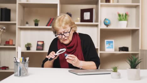 old-woman-sitting-at-the-table-examines-the-desk-clock-through-a-magnifying-glass