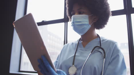 biracial female doctor wearing face mask using digital tablet