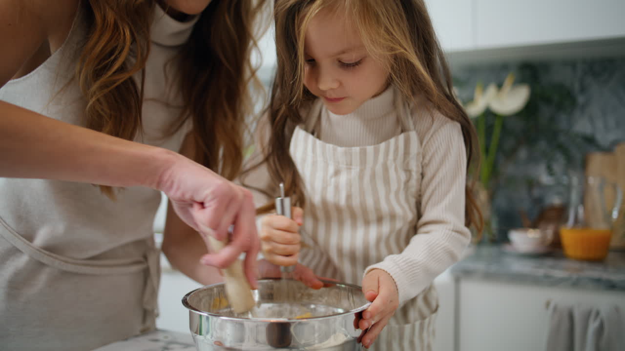Focused baby mixing whisk at kitchen closeup. Smiling mother helping to daughter