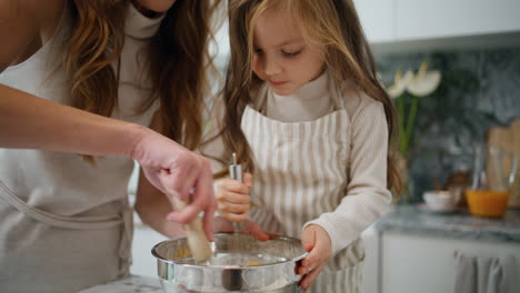 Konzentriertes-Baby,-Das-Schneebesen-In-Der-Küche-Rührt,-Nahaufnahme.-Lächelnde-Mutter-Hilft-Tochter