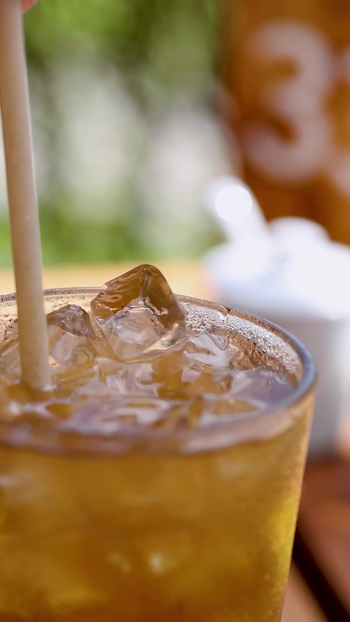 Una mano mescola una bevanda fredda con ghiaccio su un tavolo illuminato dal sole, creando una scena rinfrescante e vivace.