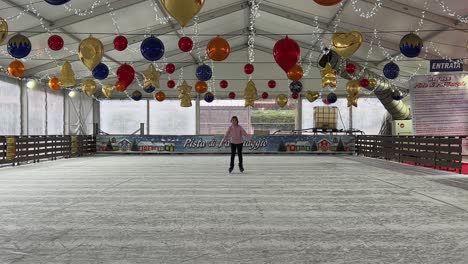 Kleines-Mädchen,-Das-Allein-Auf-Eis-In-Einer-Leeren-Indoor-Eisbahn-Mit-Weihnachtsdekorationen-Eisläuft