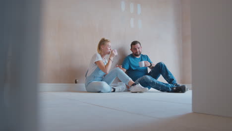 pareja decorando la habitación en casa sentada en el suelo tomando un descanso con una bebida caliente