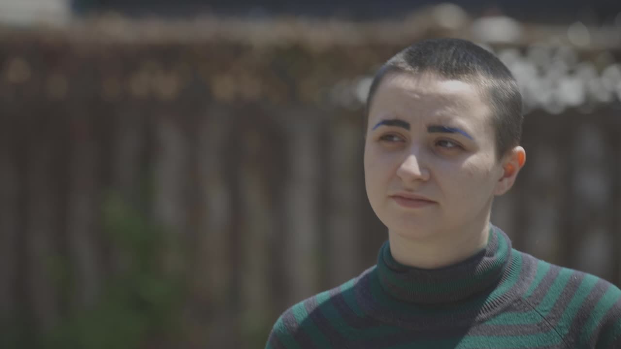 Portrait Of A Young Lesbian With Buzz Cut Hair And Gren Sweater Walking On A Hot Day. - close up shot