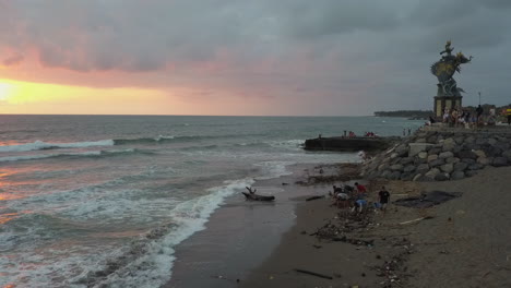 estatua de gajah mina en la playa de bali mientras los voluntarios limpian la basura de la playa