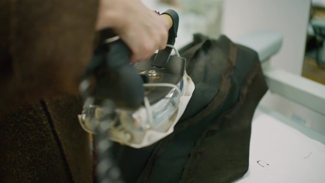 Close up of a tailor using a professional steam iron on black fabric in a fashion workshop