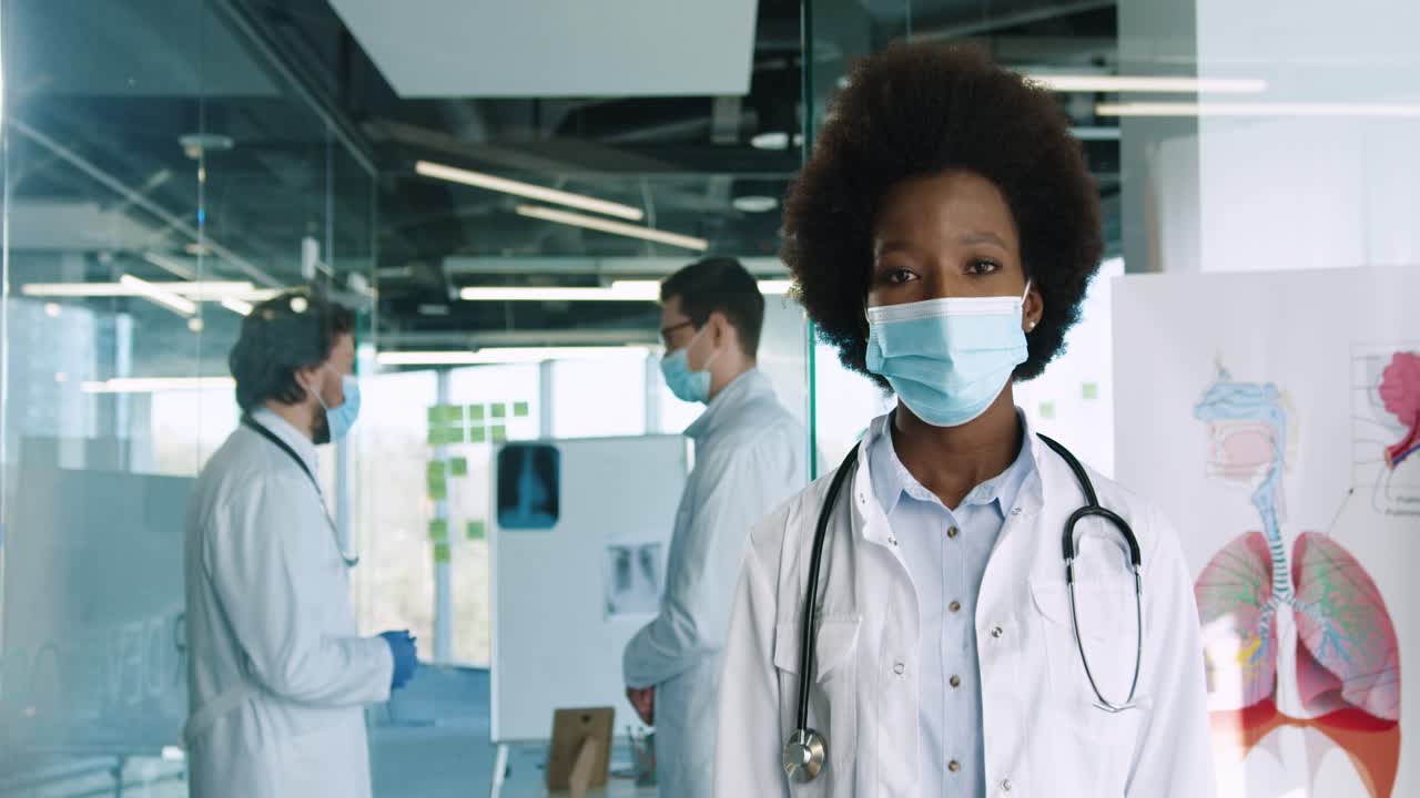 Caucasian african american female doctor in medical mask looking at camera in hospital office