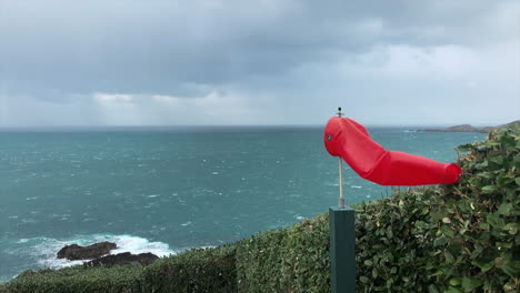 slow motion, small windsock blows at a the edge of a helipad, rain in the background falling onto the sea