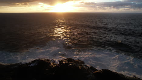 fantástica toma aérea que revela las olas rompiendo en las rocas y al atardecer