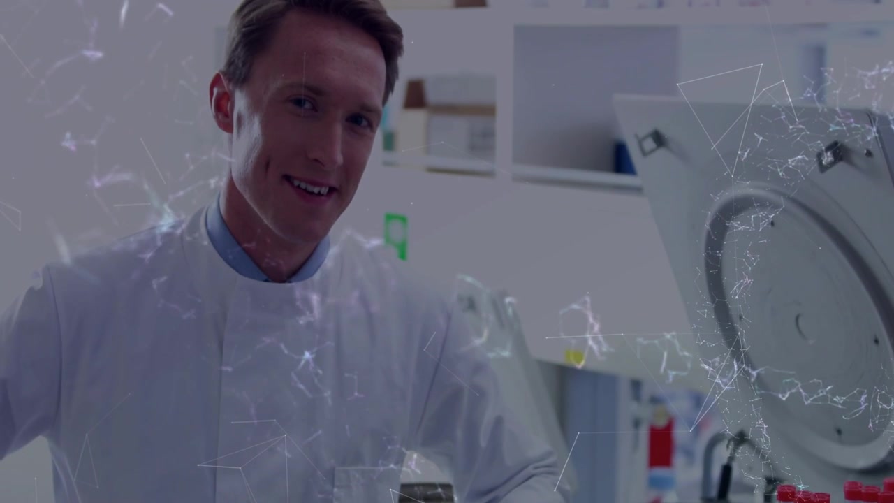 Tecnico di laboratorio uomo che gesticola e sorride mentre la telecamera si sposta verso l'alto, mostrando una centrifuga con tappi rossi.