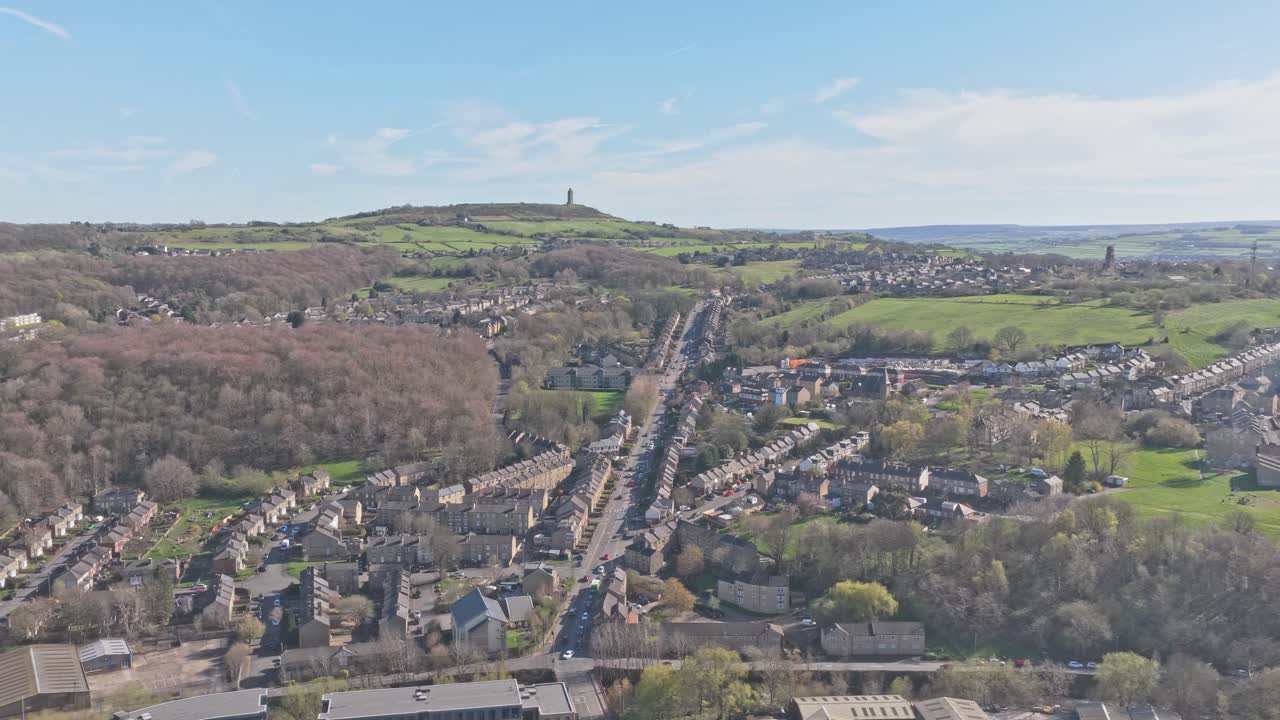 Strada A629 Wakefield che porta alla Torre Victoria di Castle Hill a Huddersfield, Kirklees, West Yorkshire, Inghilterra, Regno Unito, con case a schiera e paesaggio collinare, ripresa laterale con drone (panoramica a destra)