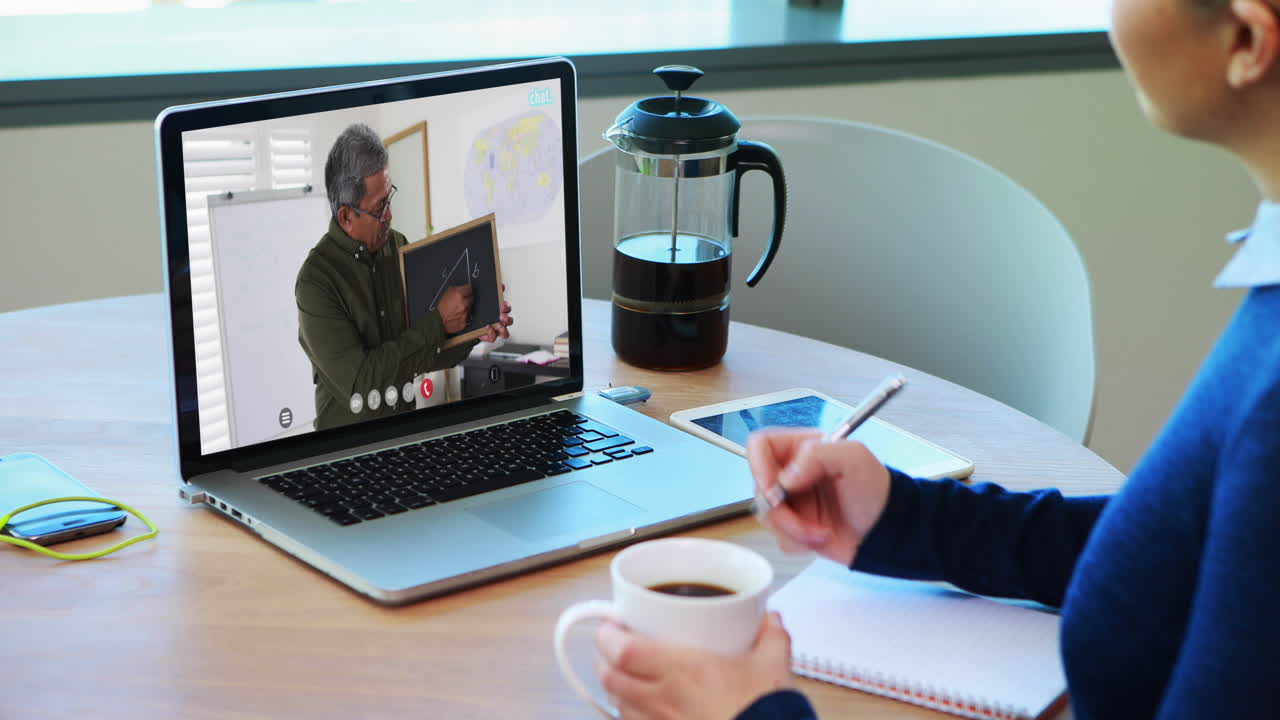 Kaukasisk kvindelig studerende bruger bærbar computer på videoopkald med mandlig lærer og tager noter.