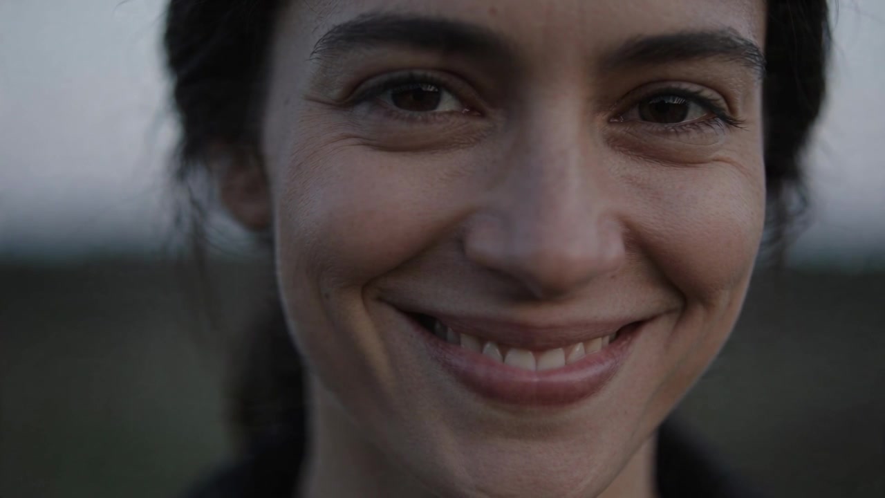 Smiling woman shifting smile into full toothy grin as camera holding close-up at dusk, dark jacket