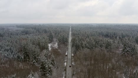 Weitblick-über-Eine-Lange,-Gerade-Straße,-Die-In-Der-Wintersaison-Durch-Einen-Wald-Führt,-Drohnenaufnahmen-In-4K,-Die-Langsam-Vorwärts-Fliegen-Und-Einem-Fahrenden-Auto-Bis-Zum-Horizont-Folgen