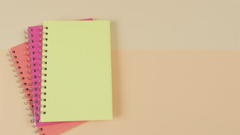 vista aérea de cuadernos de colores con espacio de copia sobre fondo beige, en cámara lenta