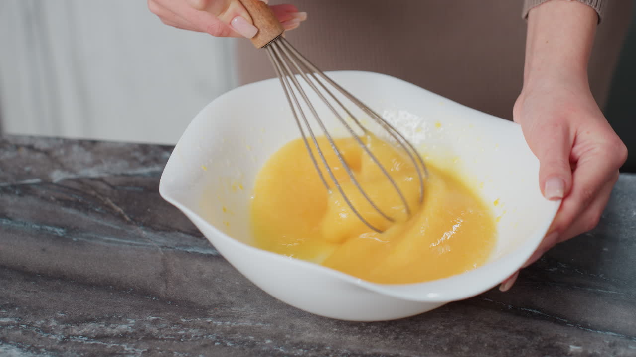 primer plano de manos golpeando huevos en un cuenco blanco en un mostrador oscuro, el borrón de movimiento captura la agitación rápida, la persona lleva ropa marrón