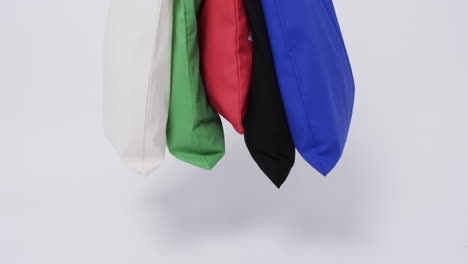 a collection of colorful tote bags in white, green, red, black, and blue hangs against a plain backg