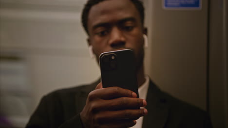 close up of young businessman in suit commuting to work sitting in london underground tube train wearing wireless earbuds to stream from mobile phone shot in real time