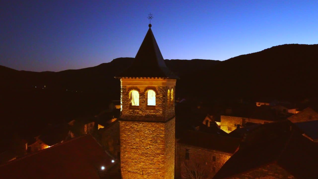 vuelo orbital sobre una iglesia en un pueblo de montaña en los pirineos españoles al atardecer