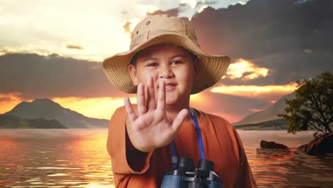 niño asiático con un sombrero y binoculares usando la lupa, mostrando la mano sin gesto en un lago. niño investigador, aventura de turismo de viaje, primer plano