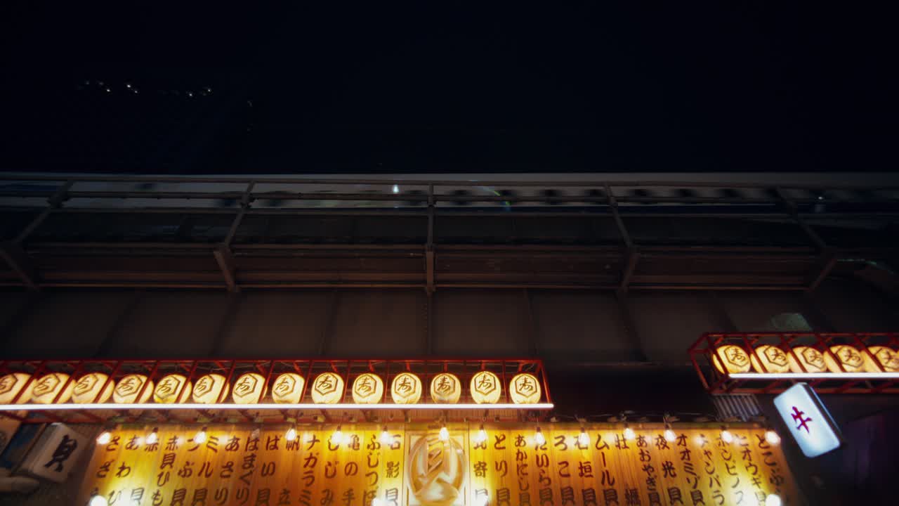 Night view of a Japanese city street with a passing train and illuminated restaurant