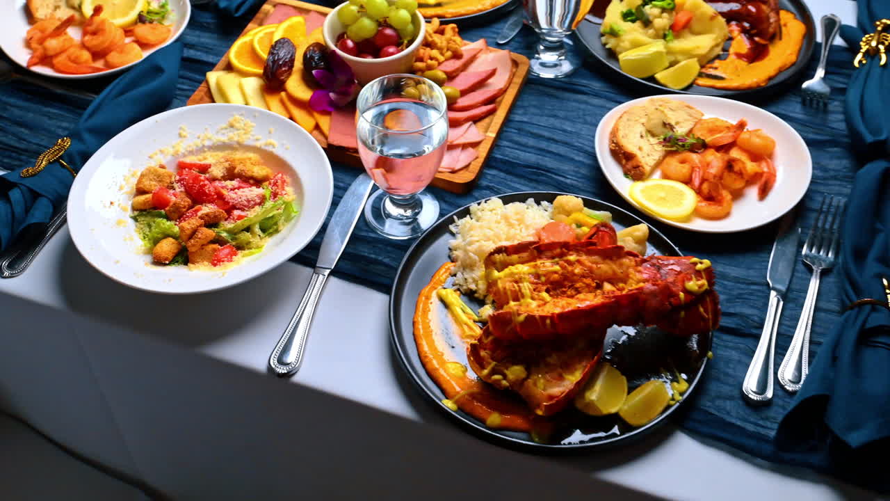 Lobster tail and assorted gourmet food on table. High angle view of cooked lobster tail with rice, Caesar salad, cheese platter, and shrimp on blue tablecloth