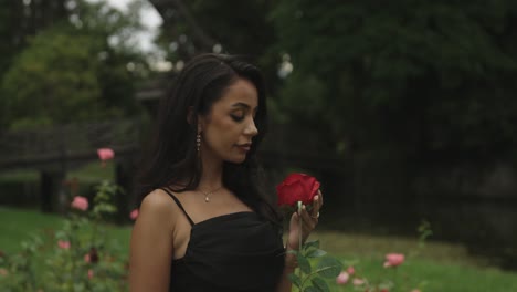 Una-Mujer-Con-Un-Vestido-Negro-Y-Una-Rosa-Roja-En-La-Mano-Mira-A-La-Cámara