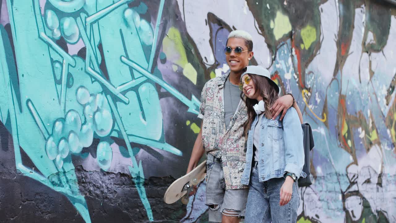 그래피티 벽 근처에서 거리를 걷고 말하는 사랑에 세련된 옷을 입은 힙스터 커플