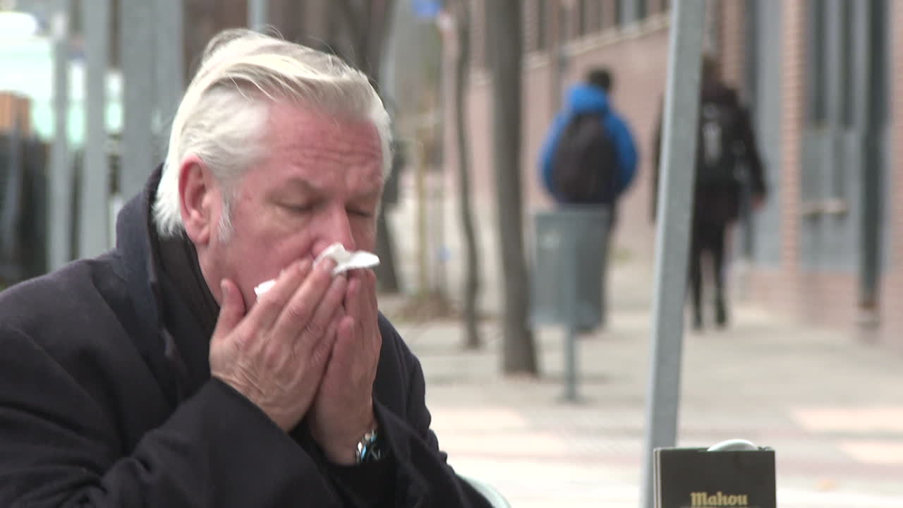 Elderly man blowing his nose outdoors
