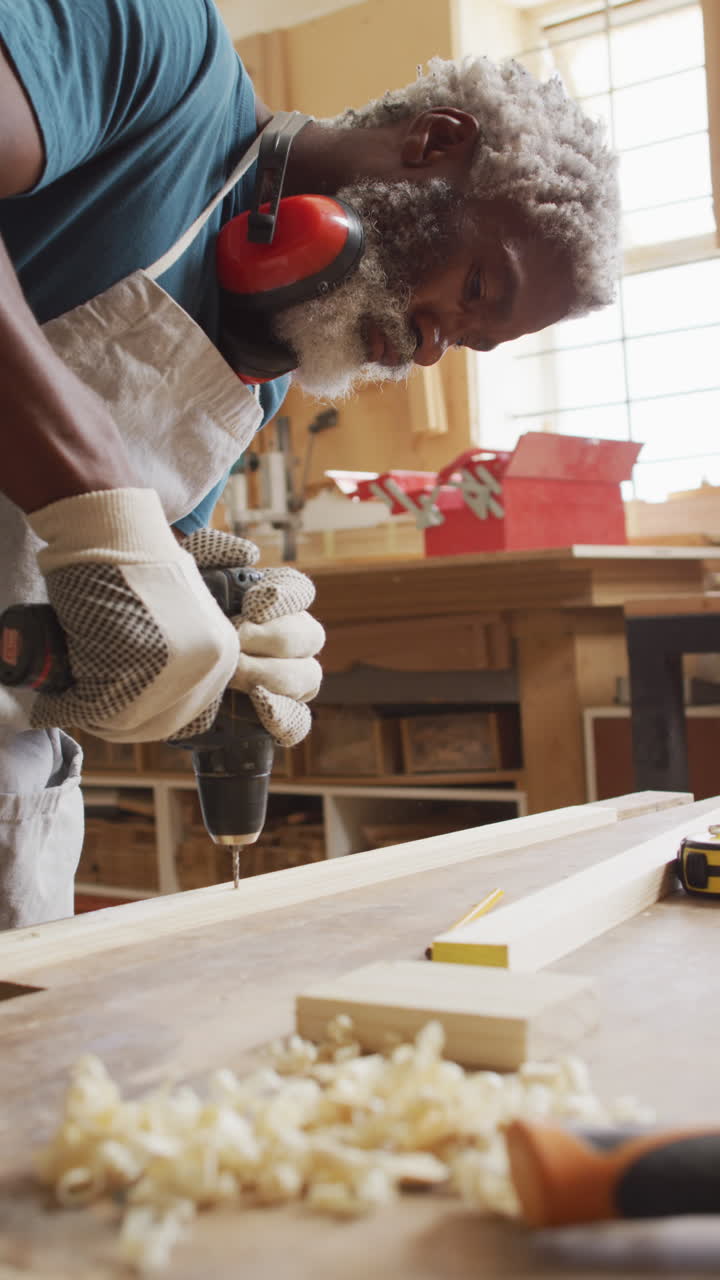 video vertical de un carpintero afroamericano de edad avanzada perforando en un taller