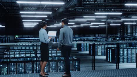 data center female system administrator and male it specialist talk, use laptop computer. information technology engineers work on cyber security network protection in cloud computing server farm.