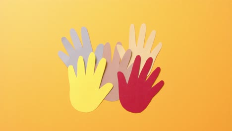 Close-up-of-hands-together-made-of-colourful-paper-on-orange-background-with-copy-space