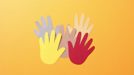 Close up of hands together made of colourful paper on orange background with copy space
